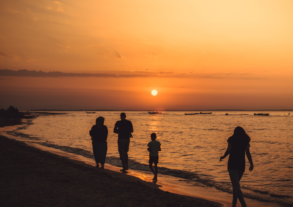 three adults and a child walking a long a beach, by the water at sunset