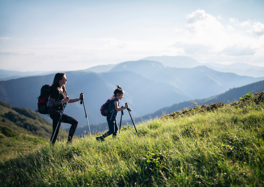 A mother and young daughter hiking up a grassy hill side