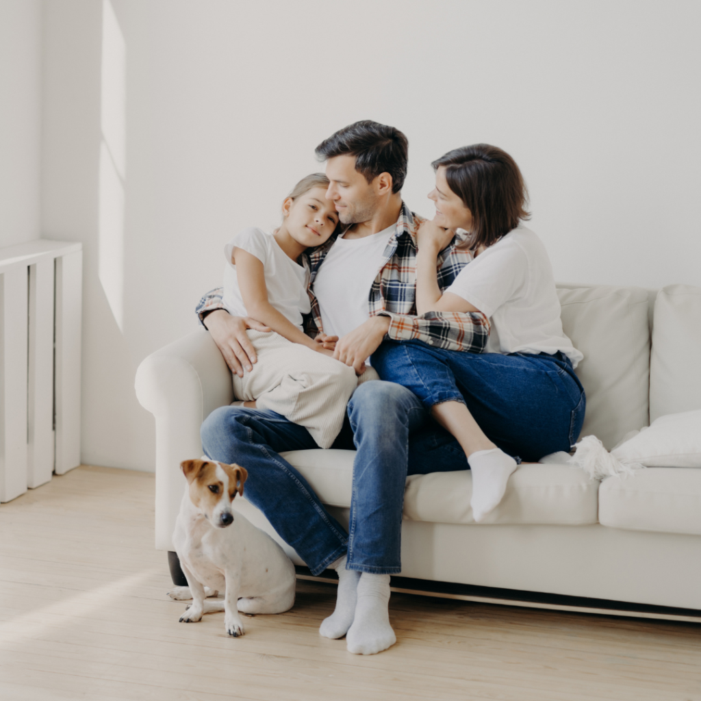 A mother, father, and daughter sat cuddling on the sofa, doting on the daughter with a dog by their feet
